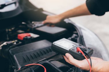 Araba tamircisi bir pil ölçer taşıyan ve motor genel durumunu denetleme.