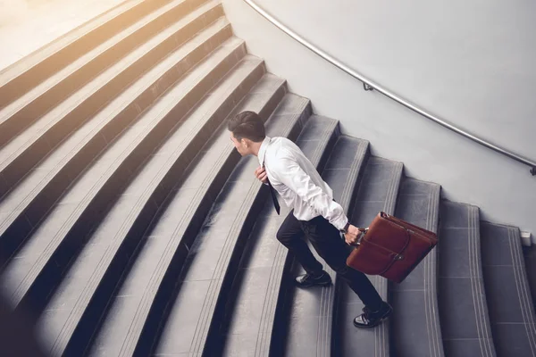 Merdivenlerde yürürken ve bavul tutan işadamı.