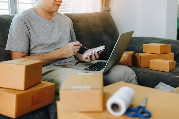 Bilgisayar dizüstü bilgisayarda bakarak ve kağıt üzerinde KOBİ kavramı sipariş listesi yazarak Genç Asyalı adam.