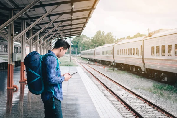 Mochila de homem asiático para viajar na estação de trem e usando tablet — Fotografia de Stock