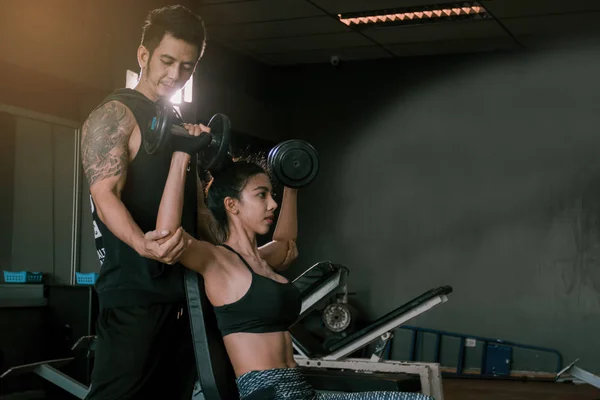 Personal trainer helping woman working lift heavy dumbbells two