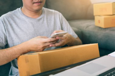 Sevk irsaliyesi evde kontrol etmek için akıllı telefon kullanan Asya genç adam.