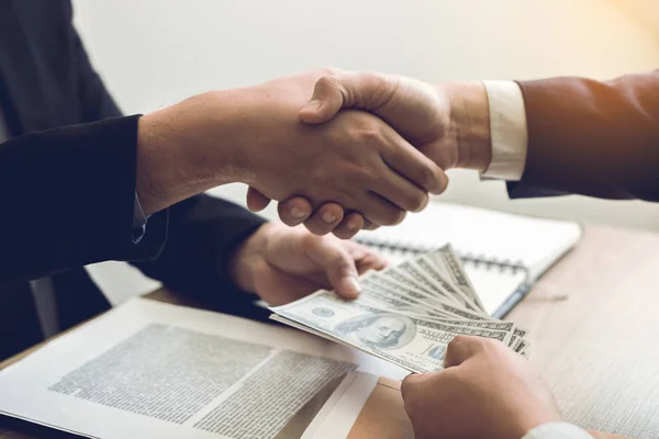 Two corporate businessmen shaking hands while one man giving mon