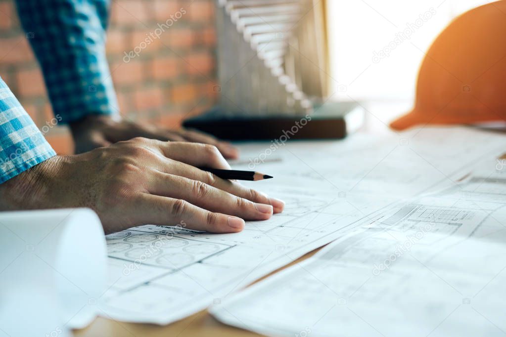 Hand of young engineering man drawing on blueprint with model on