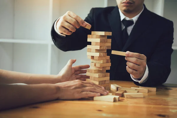 Two businessmen help to hold the wood block to fall down. — Stock Photo, Image