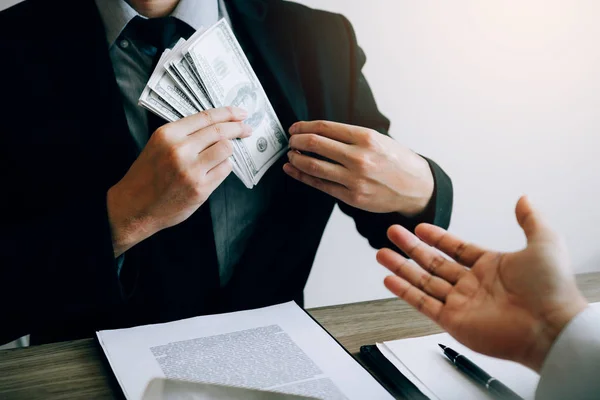 Businessman putting stack of money bills in his suit coat pocket