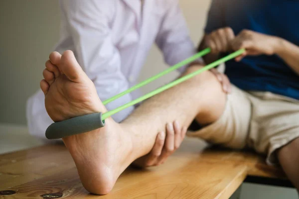 Patiënt gebruik weerstand band uitrekken zijn been met fysieke — Stockfoto