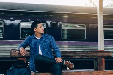 Tren istasyonunda oturan genç adam trenin kalkmasını bekliyor.
