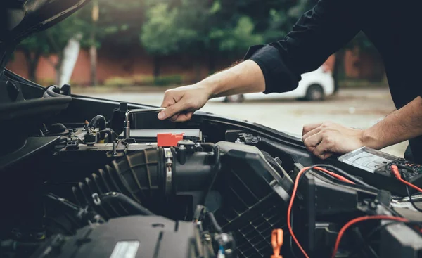 Car mechanic is checking the engine and holding the battery gaug — Stock Photo, Image