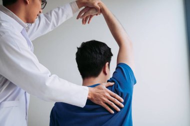 Muayenehanede genç bir adamın kolunu geren bir kayropraktik uzmanı.