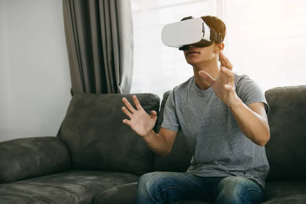 Young asian man wearing virtual reality glasses at living room f