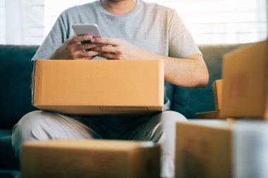 Sevk irsaliyesi evde kontrol etmek için akıllı telefon kullanan Asya genç adam.