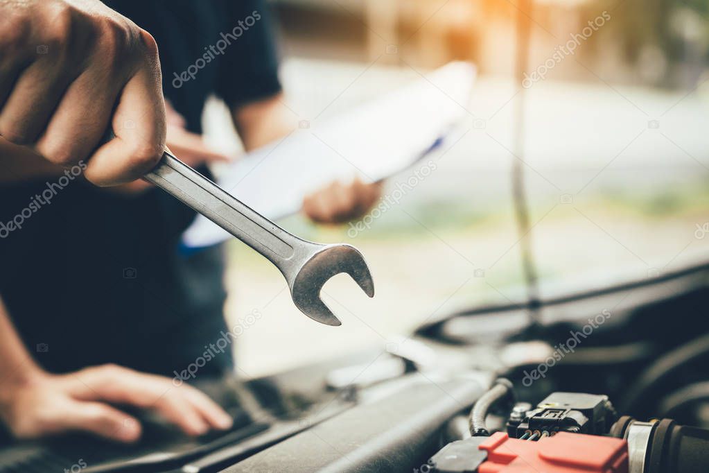 Car mechanic is holding a wrench ready to check the engine and m