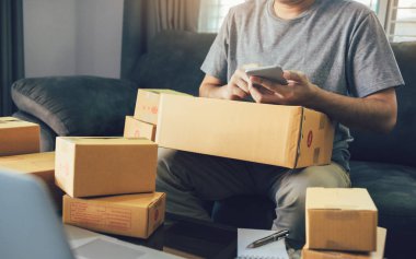 Sevk irsaliyesi evde kontrol etmek için akıllı telefon kullanan Asya genç adam.