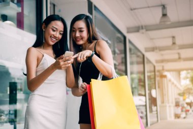 İki Asyalı kadın mağaza önünde mutlu izlerken zeki ile ayakta