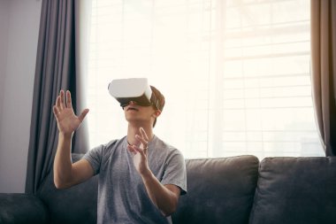 Genç Asyalı adam oturma odasında sanal gerçeklik gözlüğü giyiyor f