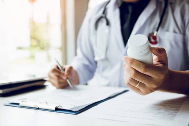 Kendine güvenen Doktor adam bir hap şişesi tutarak ve yazarak Tal