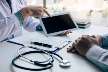 Hastanın durumunu ve tedavi sonuçlarını açıklayan tableti kullanırken Asyalı doktor hastayla konuşuyor..