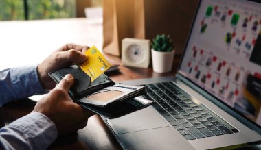 Asyalı adam, bilgisayardan online alışveriş yapmak için cebinden bir kredi kartı çıkarıyor..