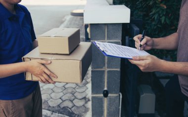 Evinin kapısında duran teslimatçı genç adam ve genç bir erkeğin imzalaması için paketler taşıyor..