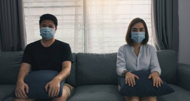 İki Asyalı çift, Coronavirus Covid-19 virüsünün yeni bir türü olan virüs salgınında sosyal uzaklık kavramından ayrı olarak evdeki koltukta oturur..
