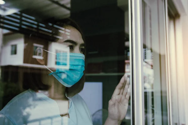 窓を通して見て 隔離された隔離されたままで病気から医療マスク保護を身に着けているアジアの女性Covid 19パンデミックウイルスマスク自宅でコロナウイルス病に対するマスク — ストック写真