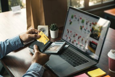 Asyalı adam, bilgisayardan online alışveriş yapmak için cebinden bir kredi kartı çıkarıyor..