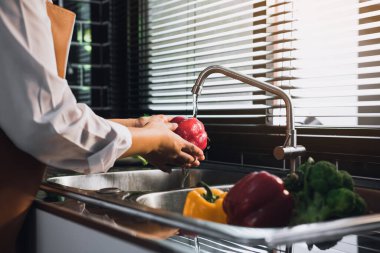 Asyalı kadın sebze yıkayan biber ve mutfakta sağlıklı yemekler hazırlıyor..