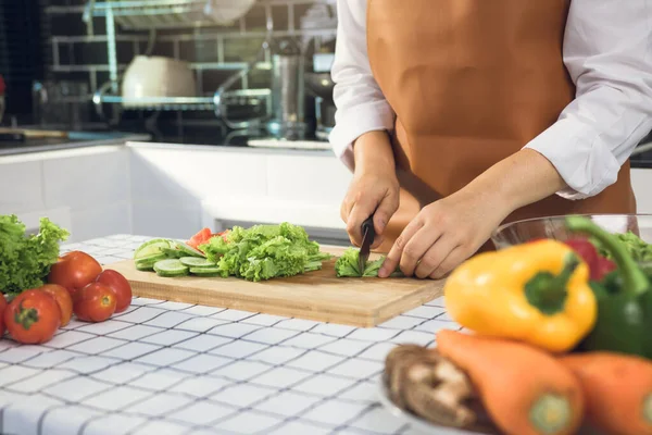 Asian woman uses a knife to cut the salad greens in the kitchen.