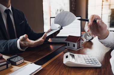 İş adamları ev satış komisyoncusu ev modelini gösteren bir kalem kullanıyor ve evin çeşitli bileşenlerini tarif ediyor..