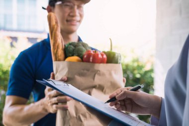 Asyalı kadın ürünü kontrol ediyor ve sipariş makbuzunu online süpermarketten imzalıyor..
