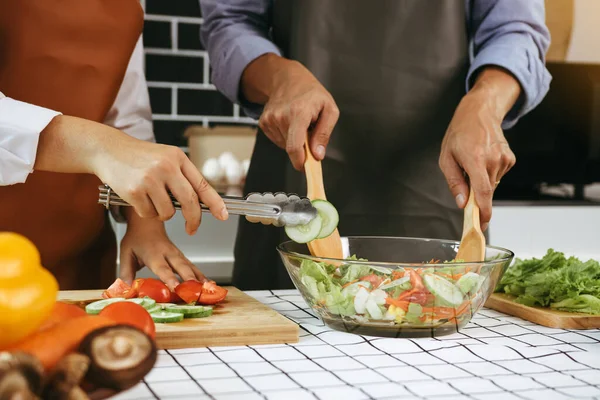 Asian couple preparing healthy salad in the kitchen.