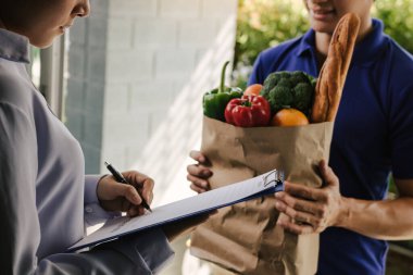 Asyalı kadın ürünü kontrol ediyor ve sipariş makbuzunu online süpermarketten imzalıyor..