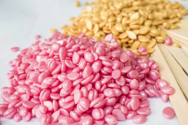 beyaz bir arka plan üzerinde tanecikler pembe ve altın balmumu ve Depilasyon için ahşap sopa vardır.