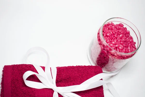 Beyaz bir arka plan üzerinde izole bir cam kavanoz Depilasyon için kırmızı toz balmumu ile ve beyaz bir yay ile kırmızı havlu olduğunu.