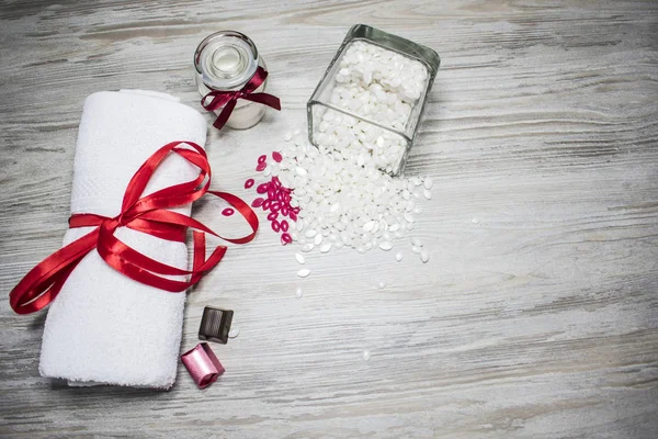 Gri wood bir arka plan üzerinde beyaz balmumu, kırmızı bir yay, bir mum ve çikolata ile beyaz bir havlu ile bir kavanoz olduğunu.