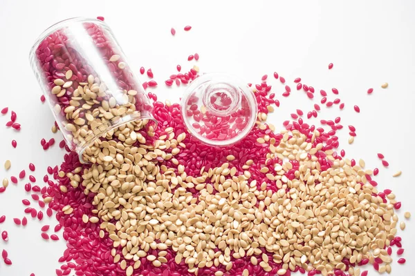 Kırmızı ve altın renkli granüller cam bir kavanozdan dökülen beyaz arka planda izole edilmiş..