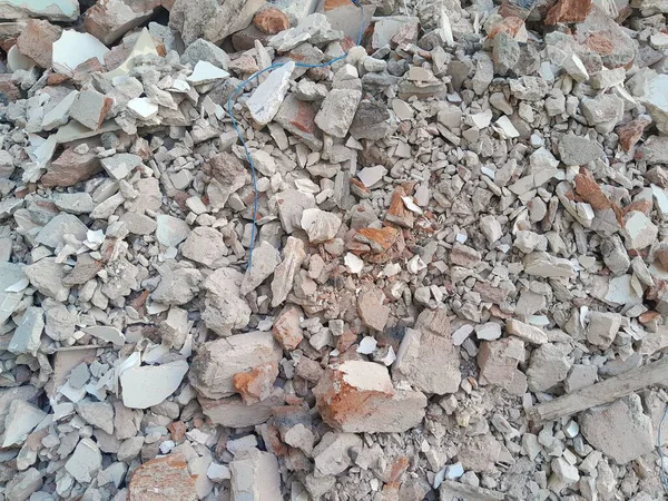 Kırık kırmızı tuğlalar ve beton parçaları. Yıkılmış bir binanın enkazı. İnşaat alanında büyük beton ve taş atığı var.
