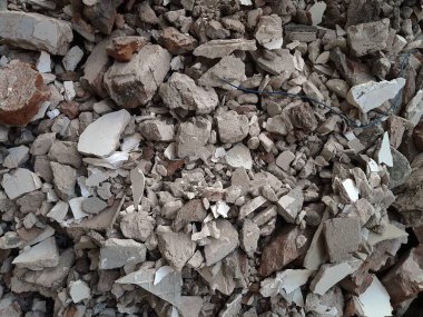 Kırık kırmızı tuğlalar ve beton parçaları. Yıkılmış bir binanın enkazı. İnşaat alanında büyük beton ve taş atığı var.