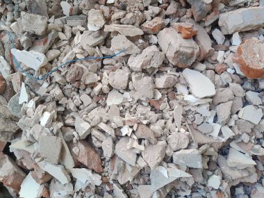 Kırık kırmızı tuğlalar ve beton parçaları. Yıkılmış bir binanın enkazı. İnşaat alanında büyük beton ve taş atığı var.