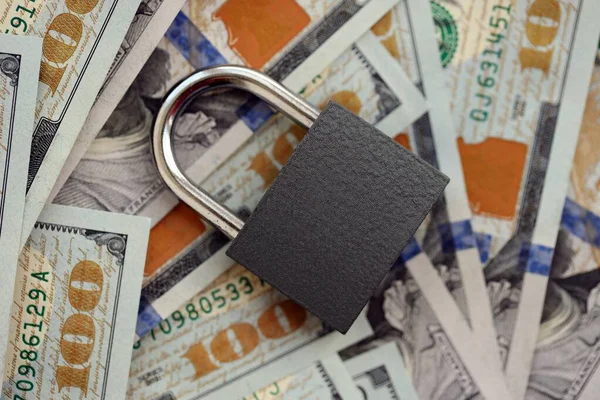 Küçük siyah asma kilit, büyük miktarlarda yeni yüz dolarlık banknotların üzerinde yatıyor.
