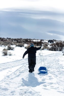 Kışın kızağı sürükleyen bir tepeye tırmanan çocuk