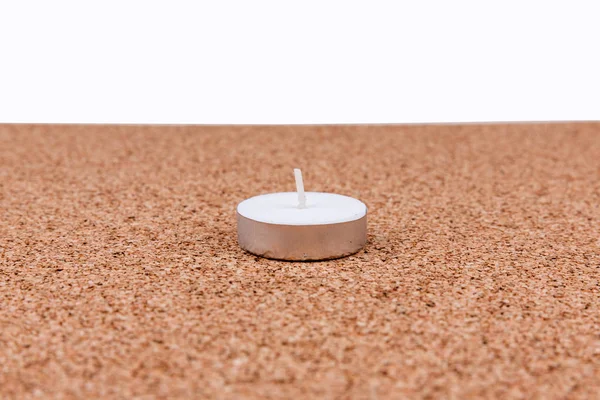 White votive candle on a plain cork board background