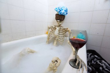 Bony skeleton taking a bubble bath in a grungy off-white dirty tub clipart