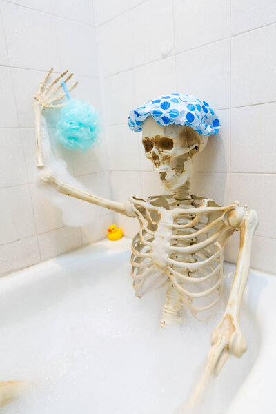 Bony skeleton taking a bubble bath in a grungy off-white dirty tub