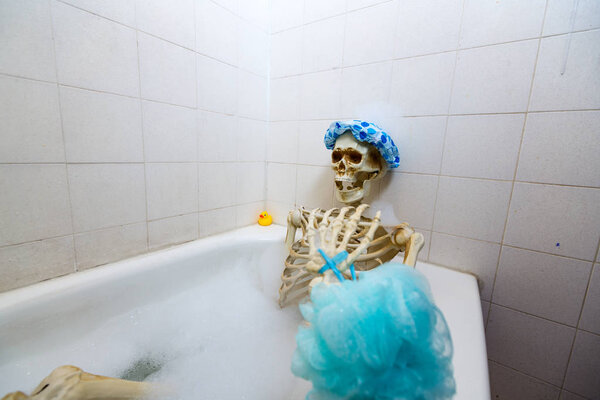 Bony skeleton taking a bubble bath in a grungy off-white dirty tub