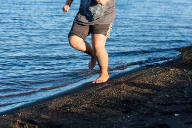 Çocuk sahilde koşuyor, suya sıçrıyor.