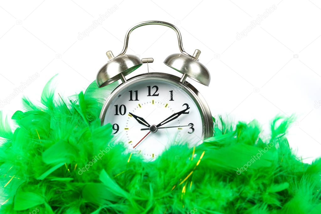 Old fashioned alarm clock wearing a green boa over white