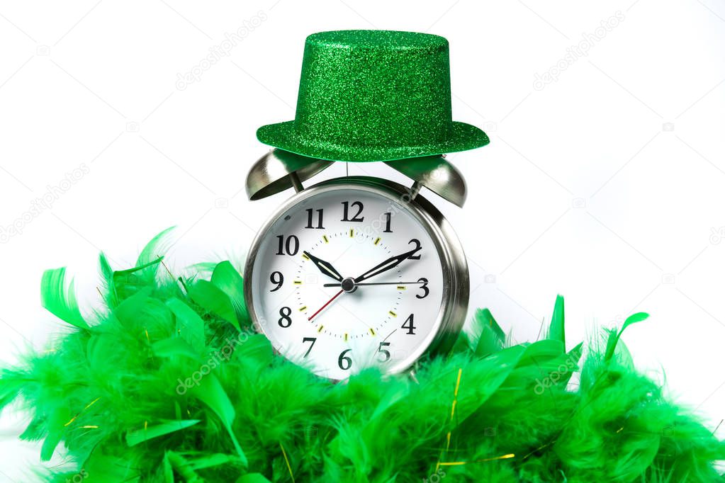 Old fashioned alarm clock wearing a green sparkly  hat and boa over white