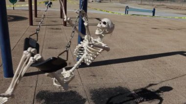 Adult skeleton in frame swinging slow motion in empty closed park 
